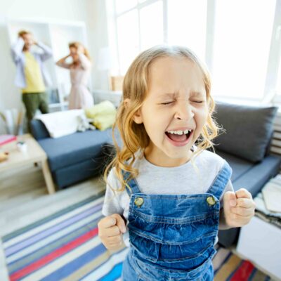 Kind in der Trotzphase schreit, während sich die Eltern die Ohren zuhalten.