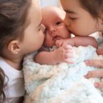 Harmonie ohne Geschwisterrivalität: Zwei ältere Schwestern küssen ein Baby.