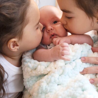Harmonie ohne Geschwisterrivalität: Zwei ältere Schwestern küssen ein Baby.